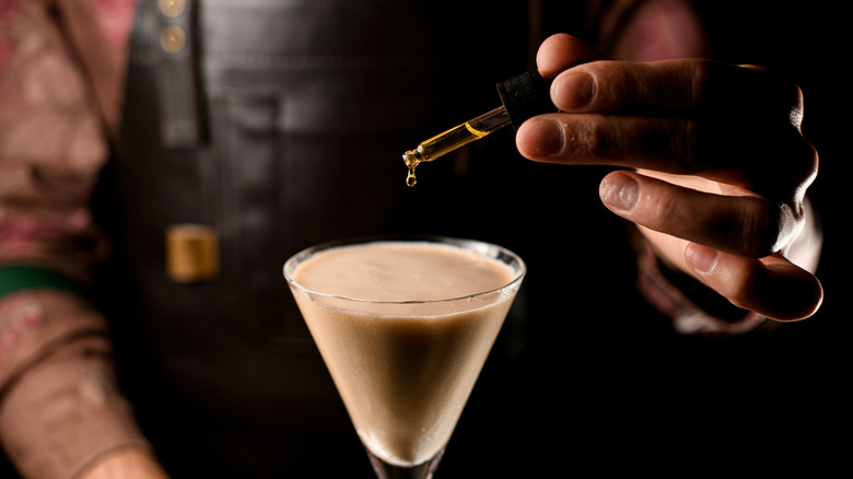 A bartender adds a few drops of bitters to a cocktail with a dropper