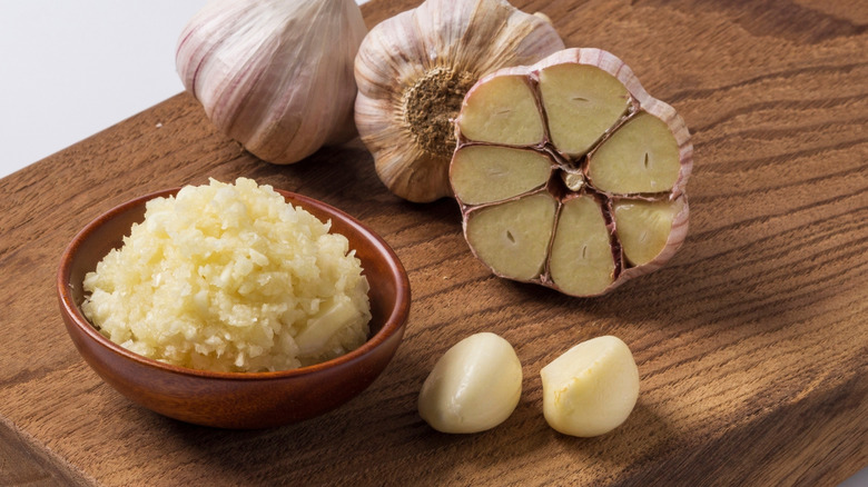 A bowl of minced garlic next to garlic cloves.