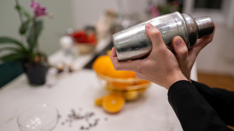 A bartender shakes a cold, silver cocktail shaker with both hands