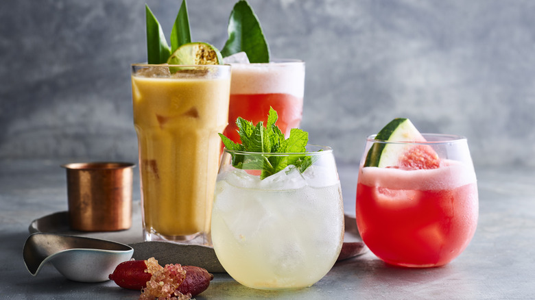 Cold cocktails with leafy garnish and drink-mixing tools on a gray background