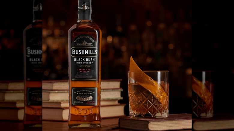 A bottle of Bushmills Black Bush with a glass of whiskey behind it
