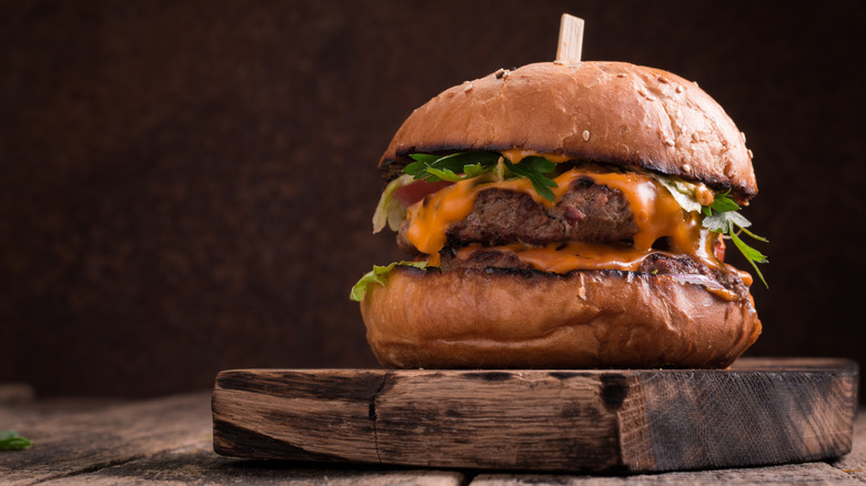 A gourmet cheeseburger sits on a wooden cutting board