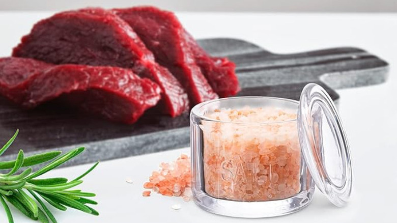 a glass salt cellar displayed on countertop next to some raw steak