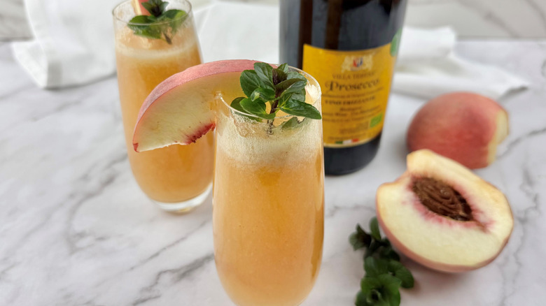 two orange-colored cocktails garnished with peach slices and mint