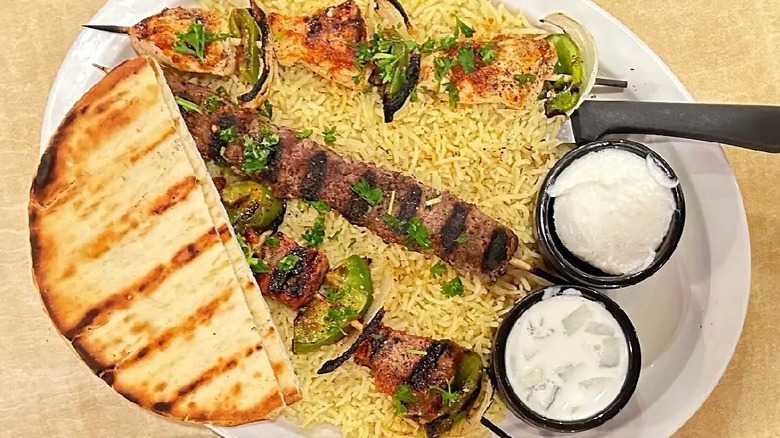 Kebabs, rice, pita bread, and dips on a white plate