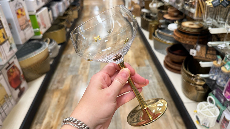 A hand holds up a wine glass with gold bows studded on it