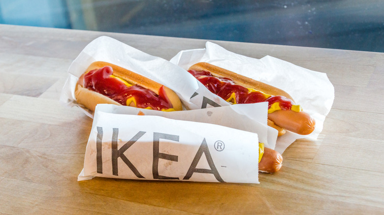 Three Ikea hot dogs with ketchup and mustard sit in their wrappers on a wooden surface