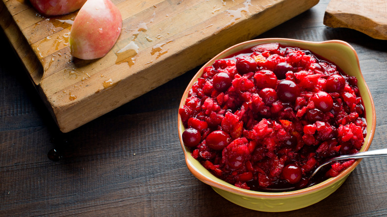 A bowl of cranberry relish sits beside slices of orange and apple