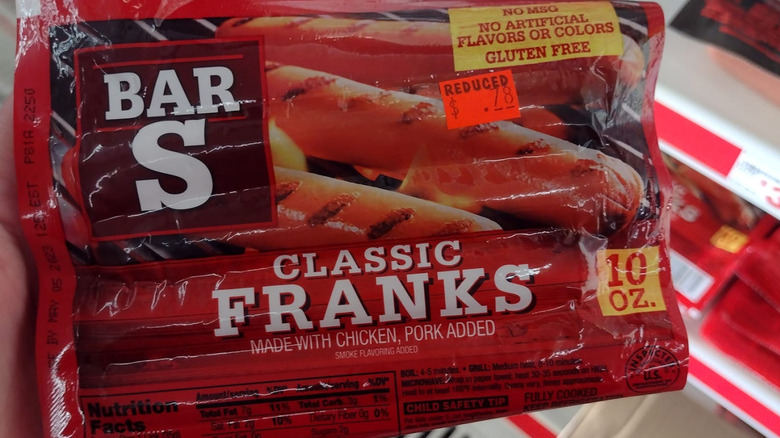 A hand holds up a package of Bar S hot dogs from Dollar Tree