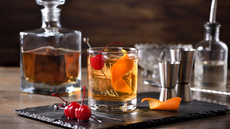 On old fashioned cocktail is garnished with a cherry and a curl of orange zest