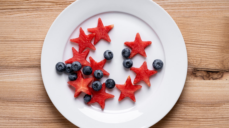 Blueberries and watermelon stars sit on a white plate against a wooden background