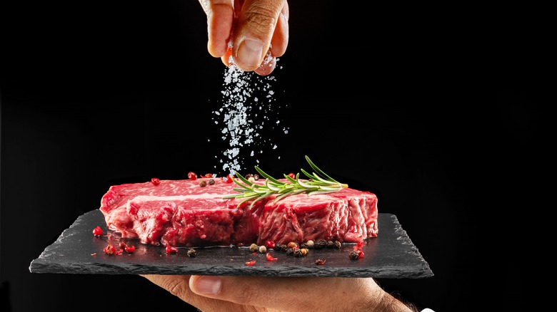 Chef sprinkling salt over a raw steak