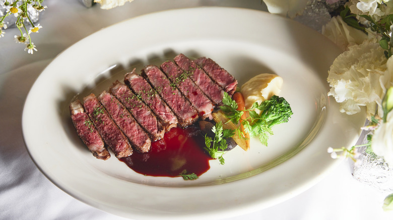 Slices of steak are arranged on a white plate with minimal accompaniments