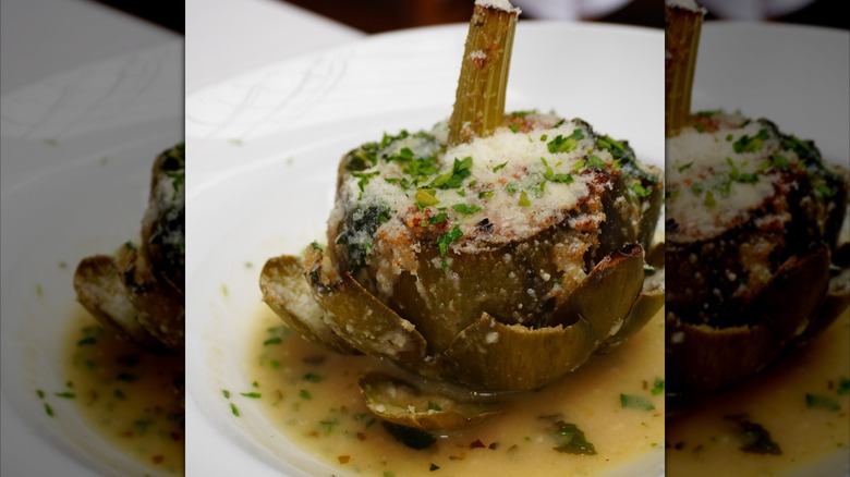 A stuffed artichoke with a heart sticking out the top is smothered in cheese and butter