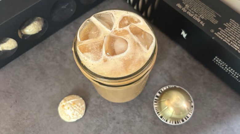 Top-down shot of iced coffee, coffee pod, latte bomb, and boxes on black surface