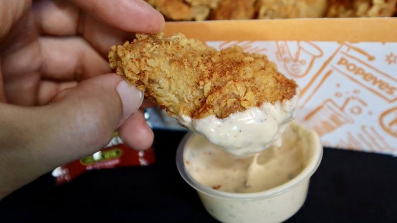 hand holding chicken wing dunked in sauce