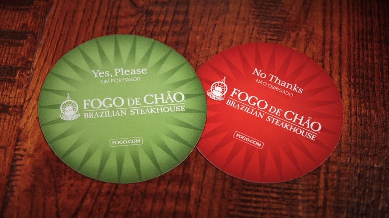 Two Fogo de Chão table cards with one flipped to the green side and the other flipped to the red side