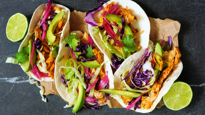 Four tacos topped with cabbage, avocado, red onion, and limes