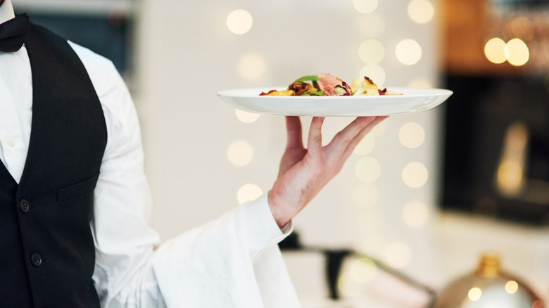 The arm of a waiter holds a steak entree on a plate in a fine dining restaurant