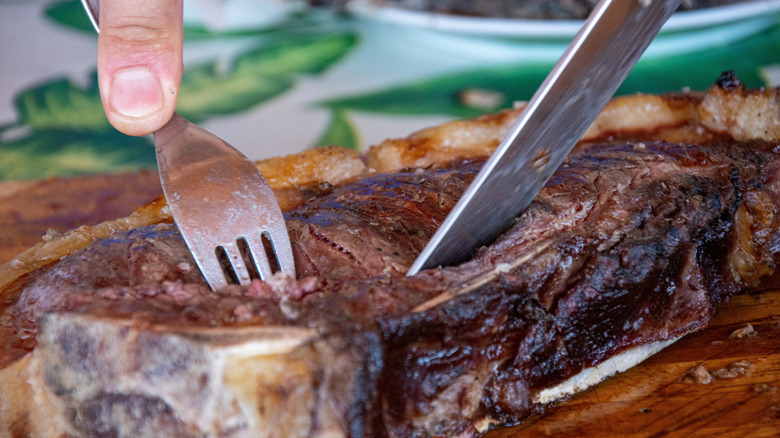 A diner uses knife and fork together to cut into a bone-in steak
