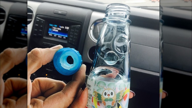 Hand holding the plastic top next to a ramune bottle with marble