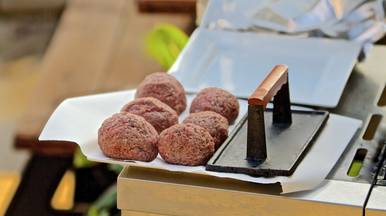 Balls of burger meat and burger press sitting on grill.