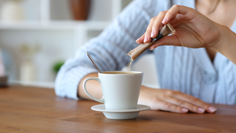 A woman pours sugar into her cup of coffee