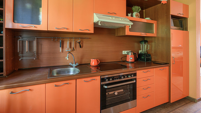 Cozy kitchen with orange cabinets, brown countertops and backsplash.