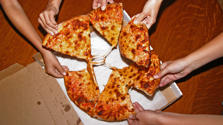 Multiple hands grabbing at a cheese pizza pie