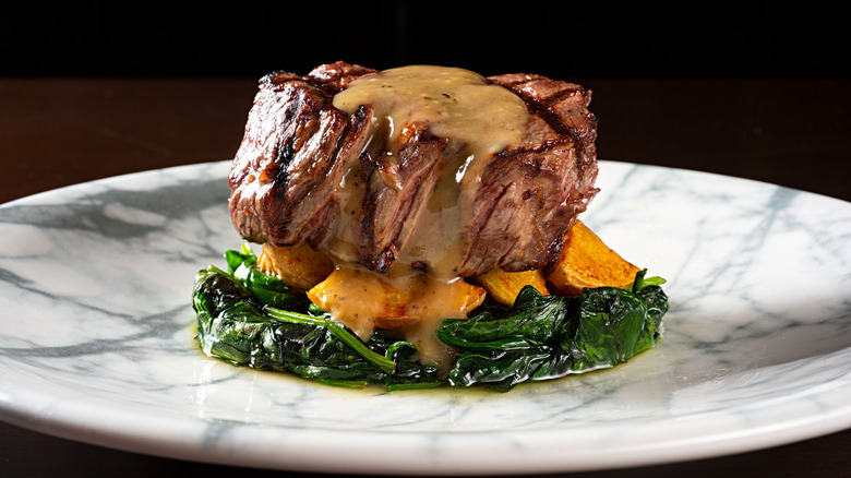 A cut of filet mignon and a bed of spinach on a white marbled plate