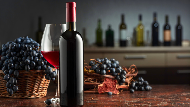 A bottle and glass of red wine with grapes