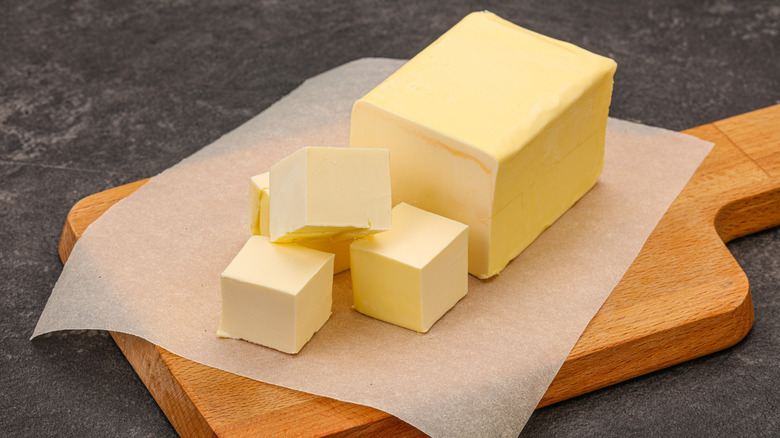 A stick of butter rests on a wooden cutting board, half-cubed