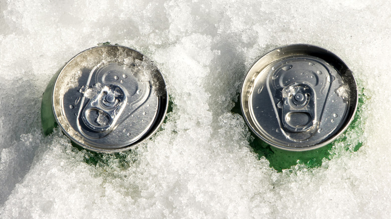 The top of two green cans of soda can be seen sitting in crushed ice
