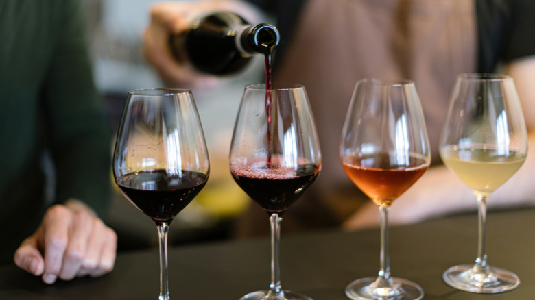 Red wine being poured into a glass alongside three other glasses of various wines.
