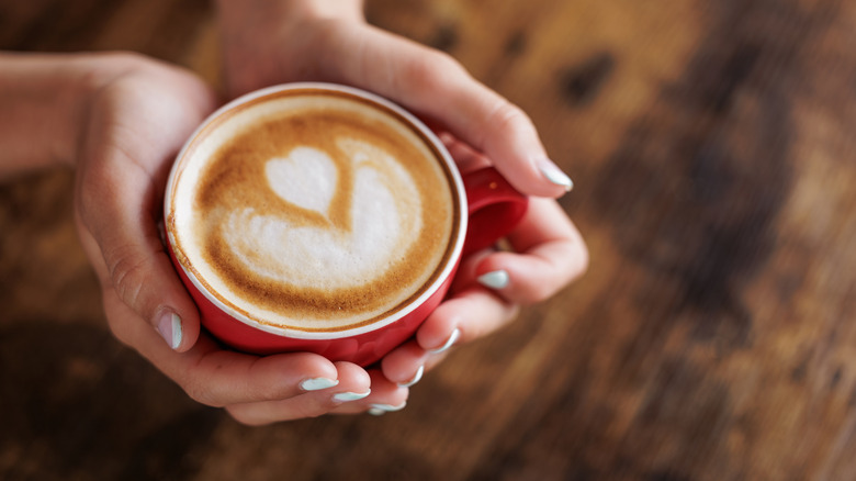 A pair of hands cupping a red coffee cup.