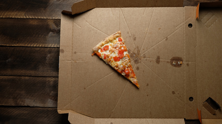 A greasy, open pizza box with a lone slice of pizza