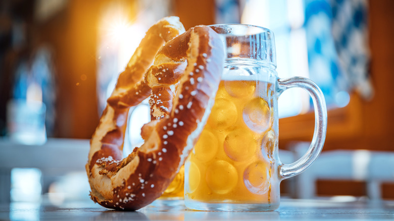Large soft pretzel with salt leaning against a large, glass beer mug of light beer