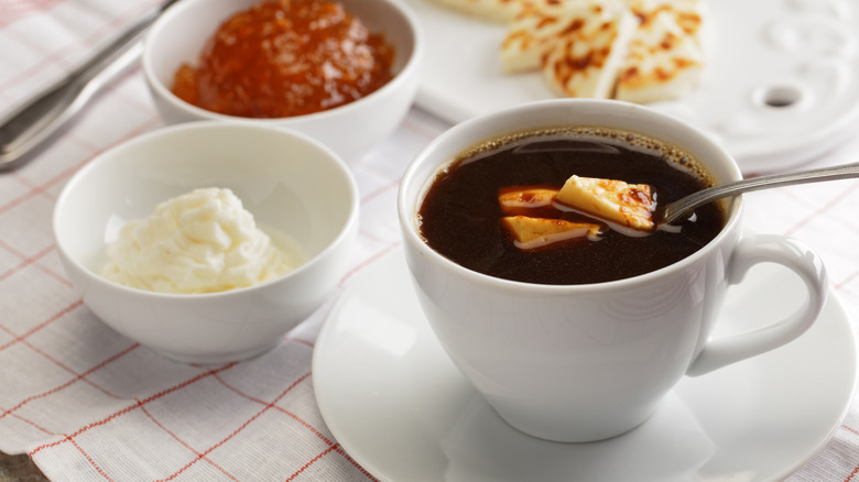 Kaffeost coffee with cheese, and sides of cheese, jam, and whipped cream, on a white and red checkered tablecloth.