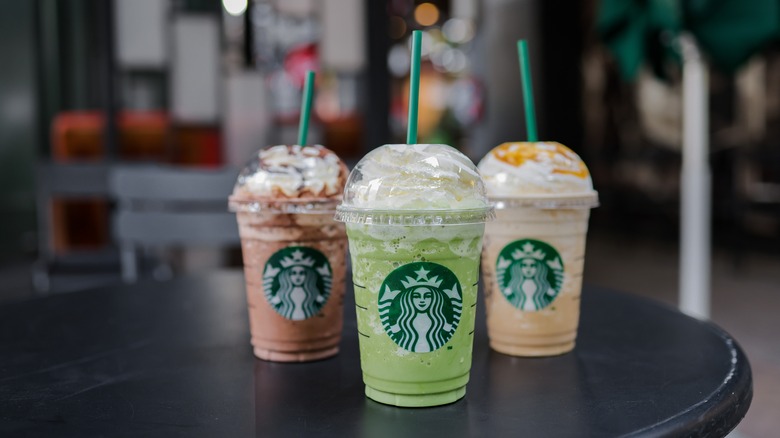 Three Starbucks Frappuccinos stand on a black table inside a cafe location