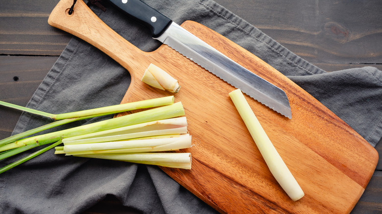 serrated knife resting on a wooden cutting board with lemongrass stalks