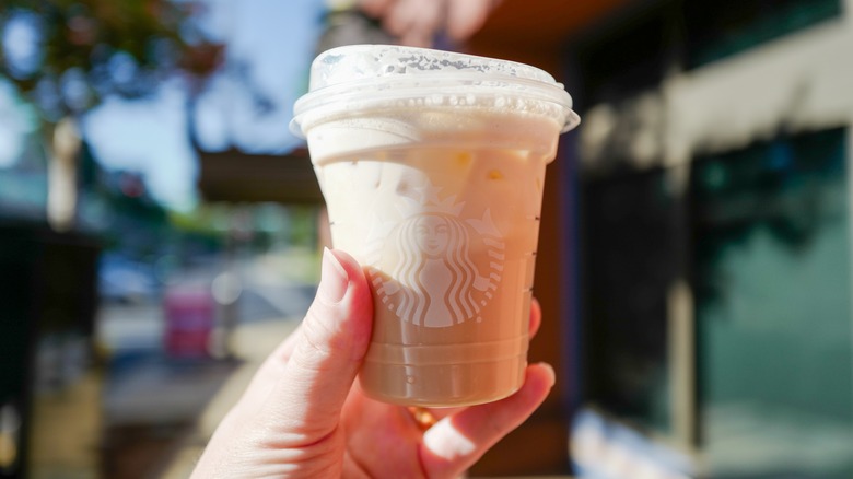A hand holds up an iced Starbucks cup in an outdoor setting