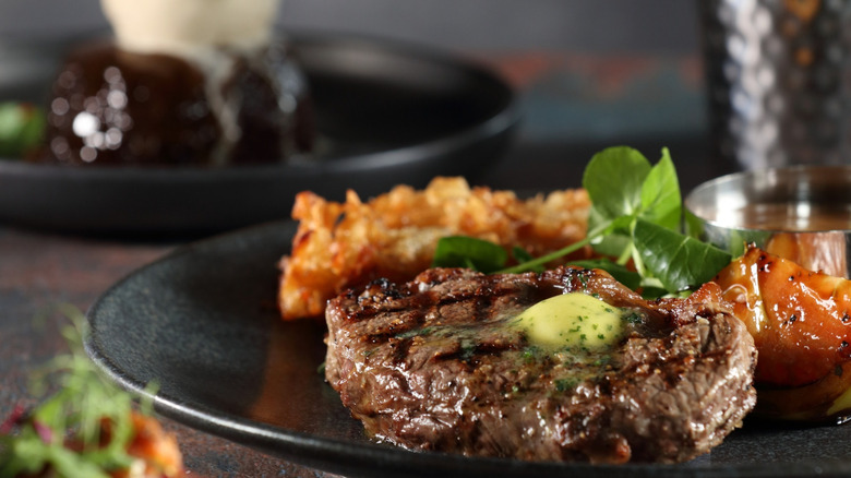 A rich 8 ounce angus steak sits next to Sticky Chipotle Chicken, grilled tomato, Sticky Toffee Pudding, and fresh greens