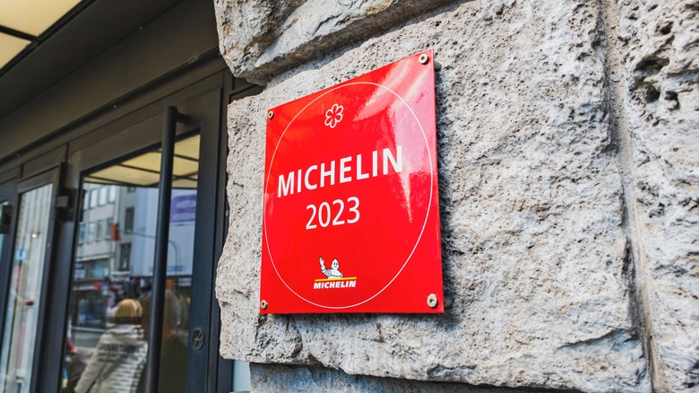 A red Michelin star sign with the year 2023 is posted on a stone wall near a doorway