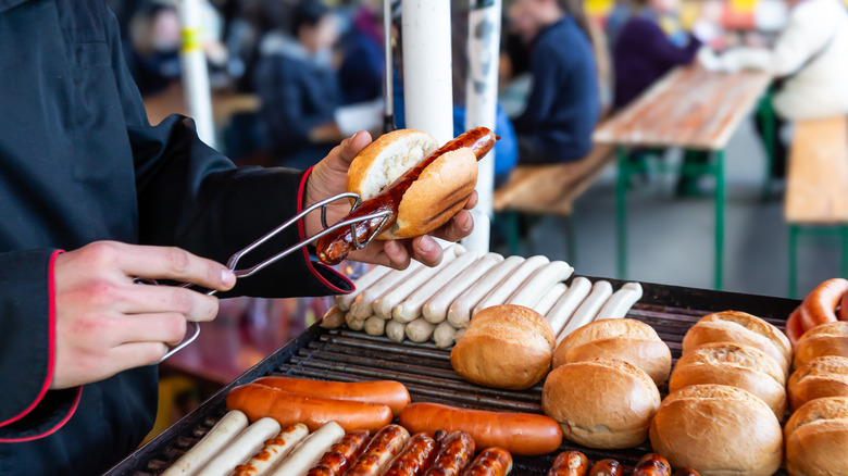 Grilled sausage being placed inside a bun