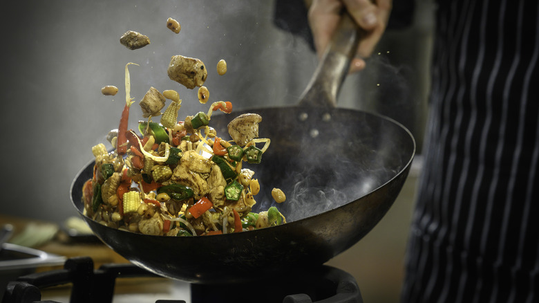 A chef using a wok to cook a stir-fry tosses the contents in the air
