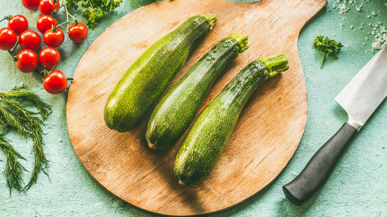 Three zucchini on a cutting board  next to a knife