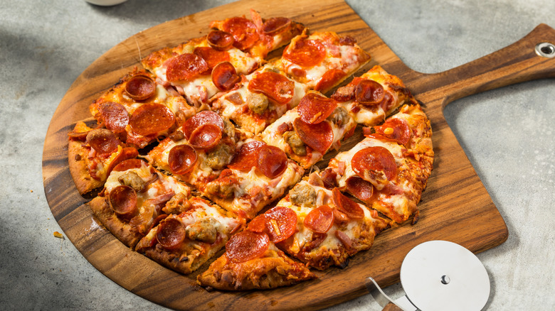 A whole tavern-style pizza sliced into squares sits on a wooden serving tray