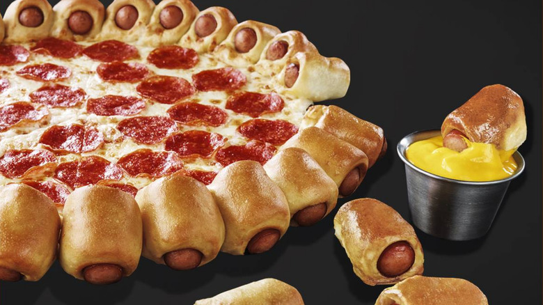 A pepperoni pizza with hot dog-filled pretzel crust, with one piece of hot dog dunked into a tub of mustard