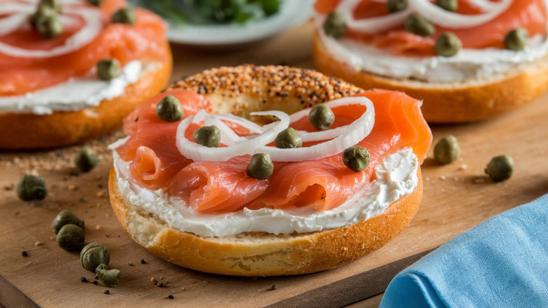 three bagels on a woodenn cutting board topped with cream, salmon, and sliced onions