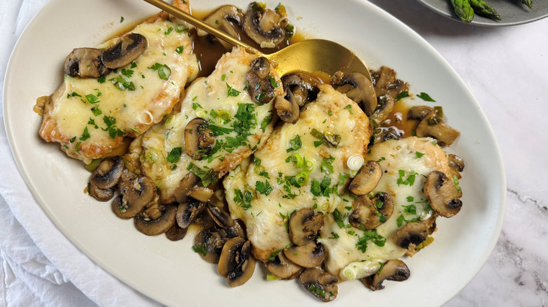 Four pieces of chicken with cheese and mushrooms on an oval plate